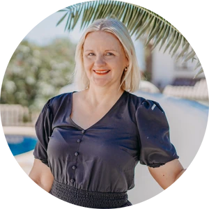 Jacy, a white woman smiling at the camera with a palm tree in the background.