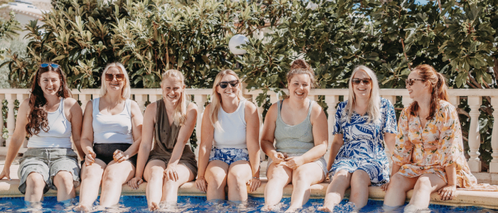 7 white women sat beside a swimming pool enjoying a small business retreat in Spain